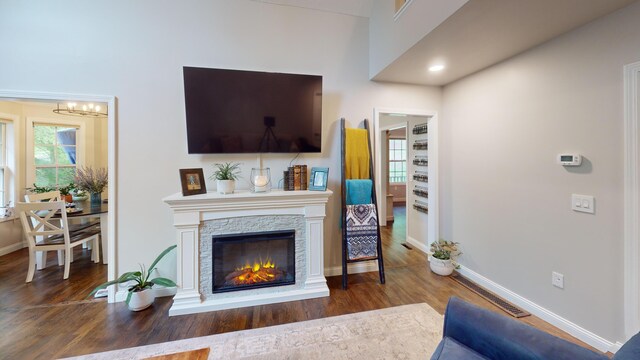 living area featuring visible vents, baseboards, wood finished floors, a notable chandelier, and a stone fireplace