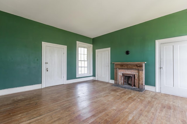 unfurnished living room featuring baseboards, wood-type flooring, and a fireplace with raised hearth