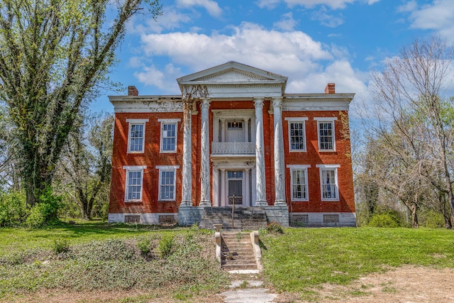 neoclassical / greek revival house with brick siding, a chimney, and a front lawn