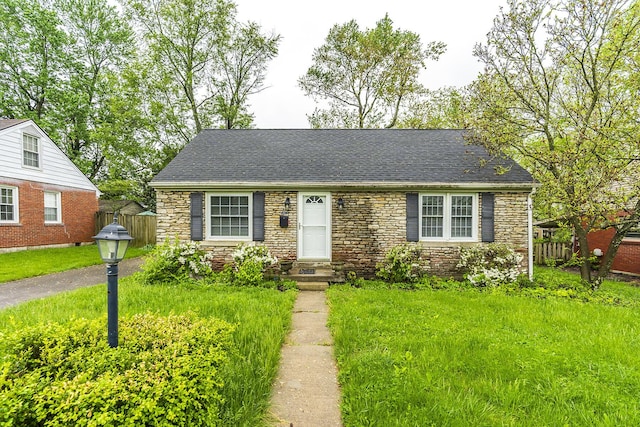 view of front of house featuring fence, roof with shingles, a front lawn, and stone siding