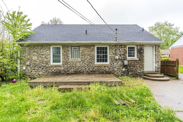 rear view of property featuring a deck, fence, roof with shingles, and stone siding