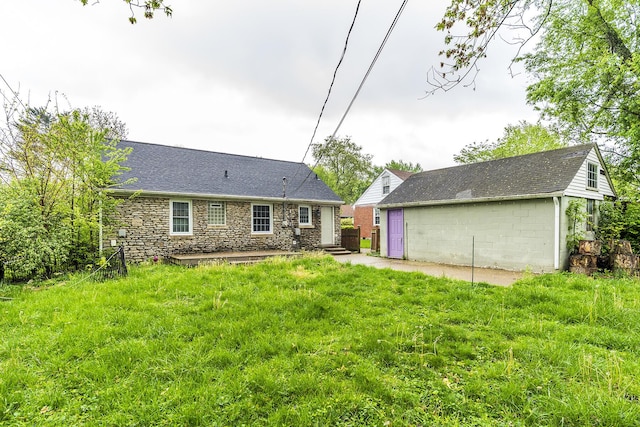 back of house with a lawn, a patio area, a shingled roof, and stone siding