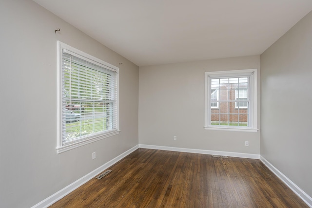 empty room with visible vents, dark wood-style flooring, a wealth of natural light, and baseboards