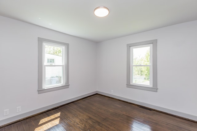 unfurnished room with visible vents, dark wood-style floors, and baseboards