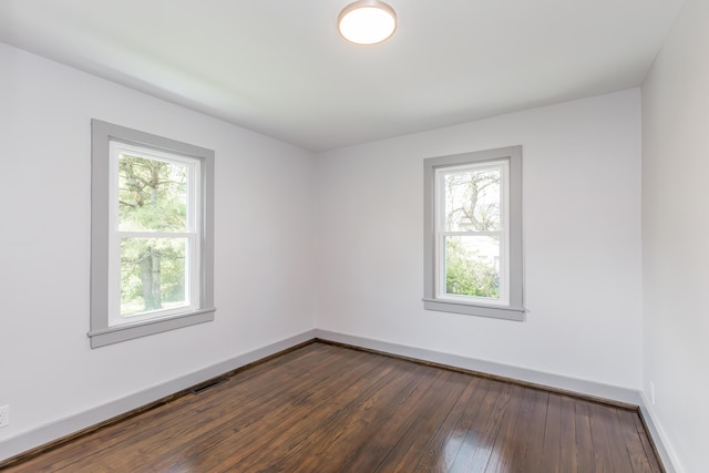 empty room with dark wood-style flooring, baseboards, and visible vents