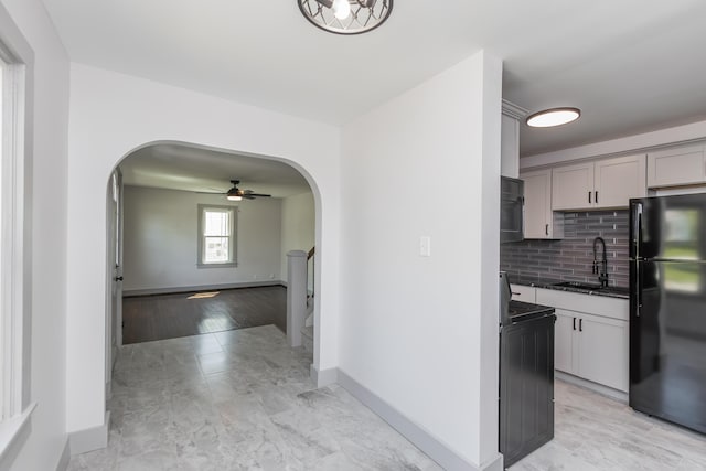 kitchen with a sink, ceiling fan, freestanding refrigerator, arched walkways, and gray cabinets