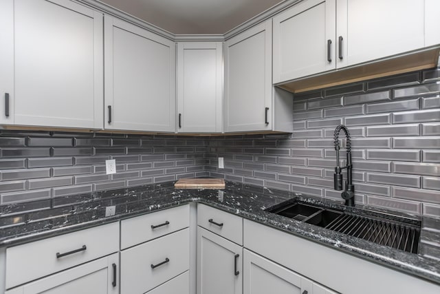 kitchen featuring dark stone countertops, tasteful backsplash, and a sink
