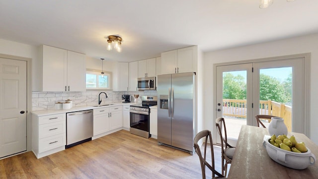 kitchen with white cabinets, a sink, light countertops, stainless steel appliances, and decorative backsplash