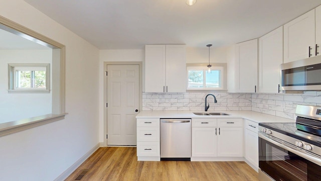 kitchen featuring light wood-style floors, a sink, decorative backsplash, and appliances with stainless steel finishes