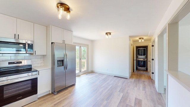 kitchen featuring stacked washer and dryer, appliances with stainless steel finishes, light countertops, light wood-type flooring, and tasteful backsplash
