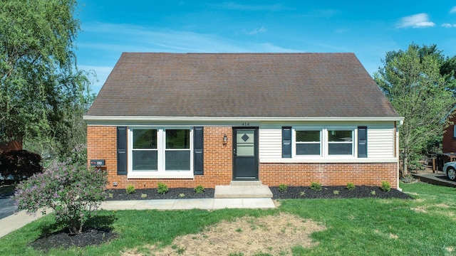 new england style home with brick siding, a shingled roof, and a front lawn