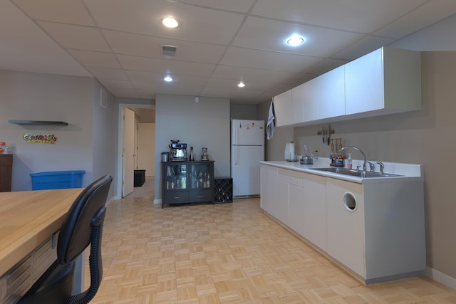 kitchen featuring white cabinetry, a sink, visible vents, freestanding refrigerator, and baseboards