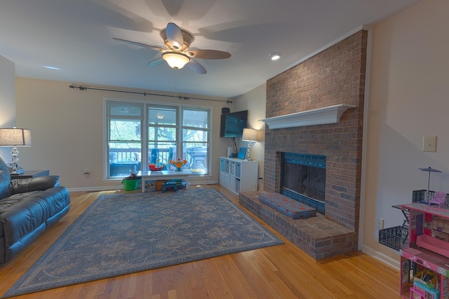 living area with baseboards, wood finished floors, a ceiling fan, and a fireplace