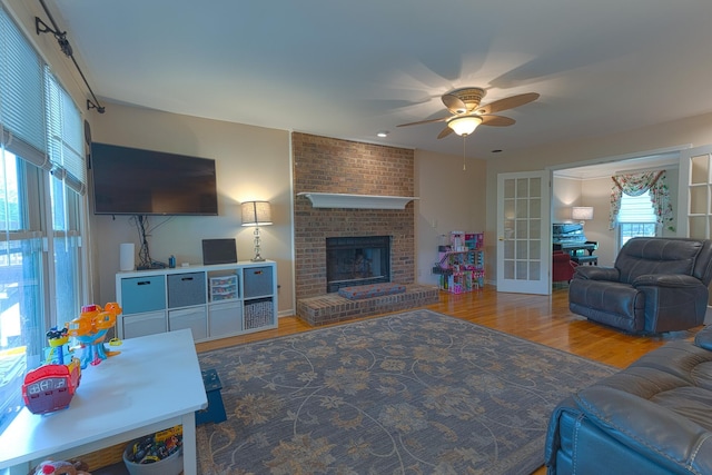living area featuring wood finished floors, ceiling fan, french doors, and a brick fireplace