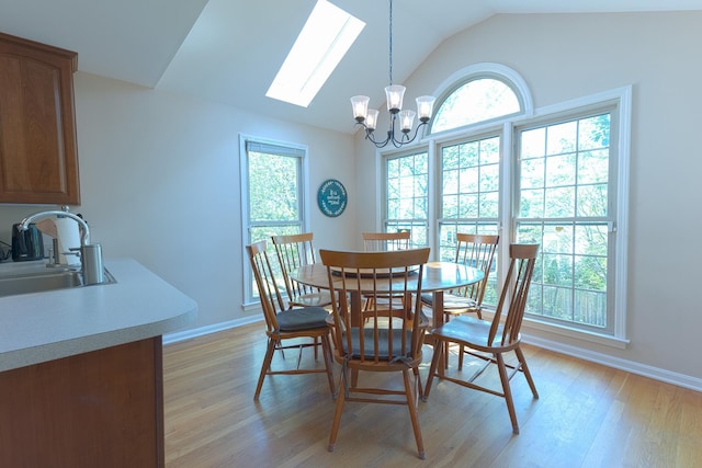 dining room with a chandelier, baseboards, vaulted ceiling with skylight, and light wood finished floors
