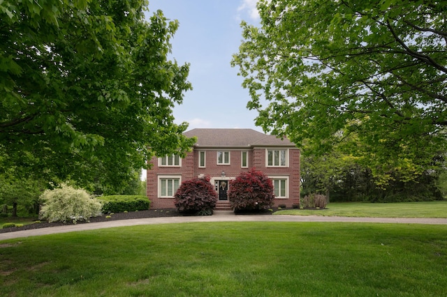 colonial house with curved driveway, a front lawn, and brick siding