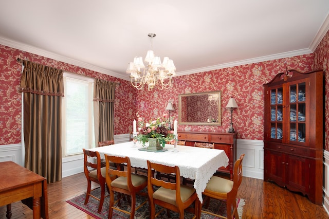 dining space featuring wood finished floors, a wainscoted wall, an inviting chandelier, ornamental molding, and wallpapered walls
