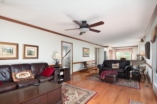living area with visible vents, ornamental molding, baseboards, light wood-type flooring, and a ceiling fan