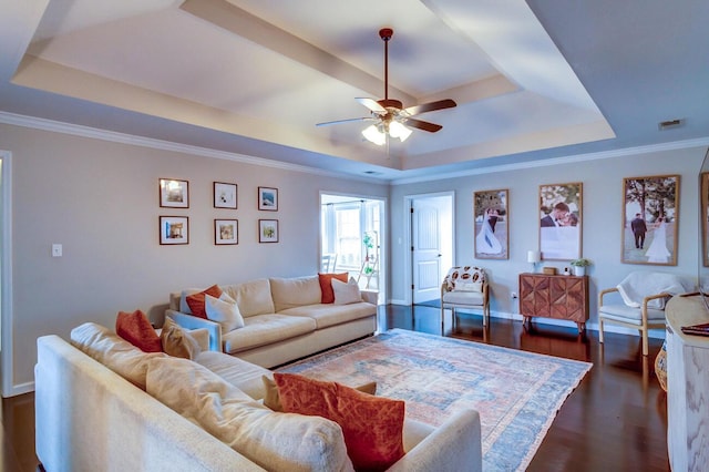 living area featuring crown molding, a tray ceiling, baseboards, dark wood-type flooring, and a ceiling fan