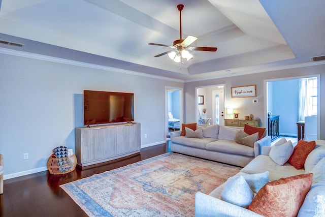 living room with visible vents, ceiling fan, a tray ceiling, baseboards, and wood finished floors