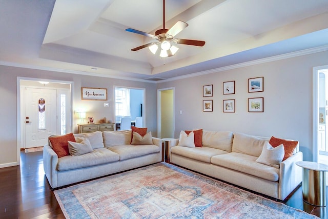 living area with a raised ceiling, baseboards, dark wood-style flooring, ornamental molding, and a ceiling fan