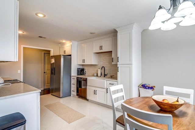 kitchen featuring decorative backsplash, stainless steel fridge, black dishwasher, a sink, and a notable chandelier