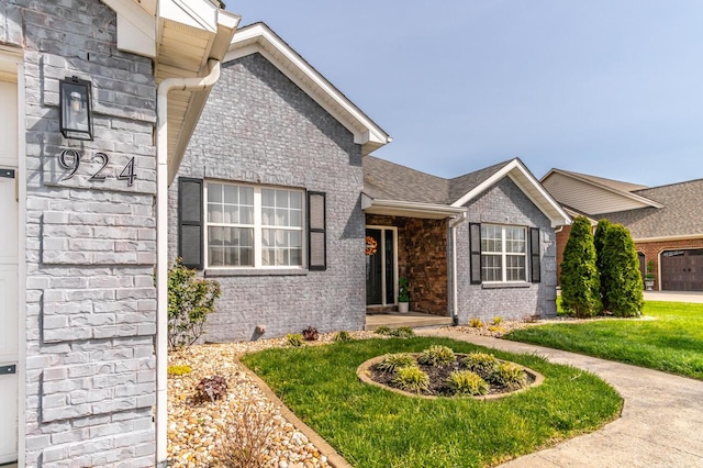 view of front of property featuring roof with shingles, a front yard, brick siding, and stone siding