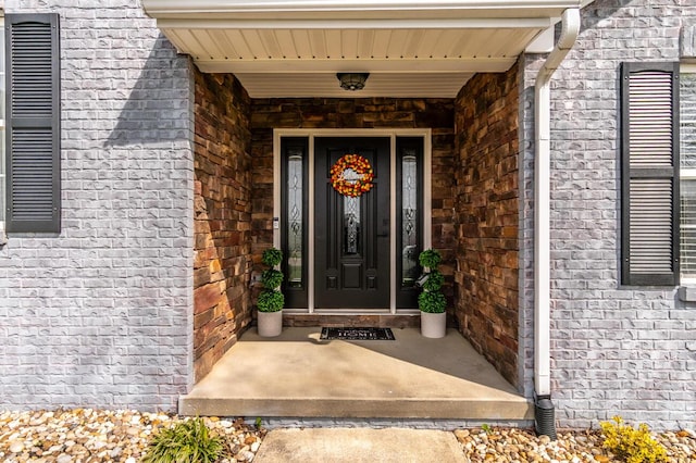 view of exterior entry with brick siding and a porch