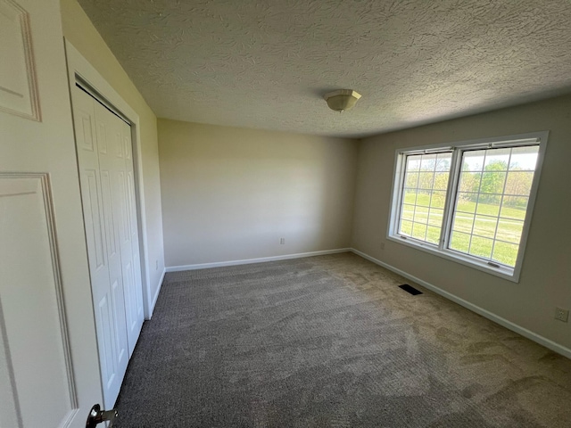 unfurnished bedroom featuring a textured ceiling, carpet, baseboards, visible vents, and a closet