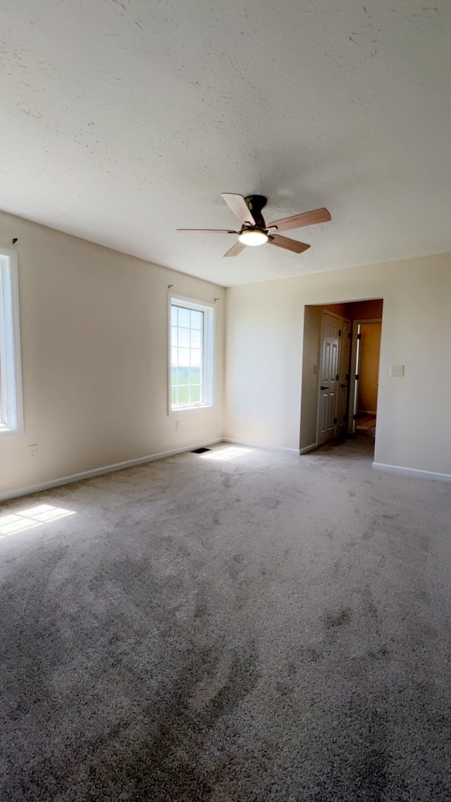 empty room featuring a textured ceiling, ceiling fan, baseboards, and carpet