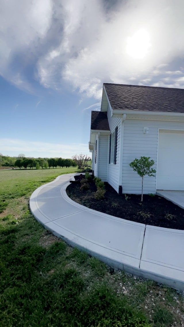 view of side of home featuring a shingled roof, an attached garage, and a lawn