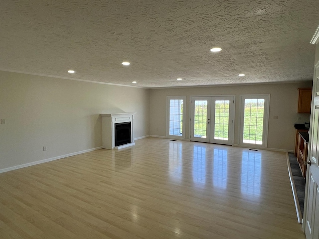 unfurnished living room with a textured ceiling, baseboards, a fireplace with raised hearth, light wood-style floors, and recessed lighting