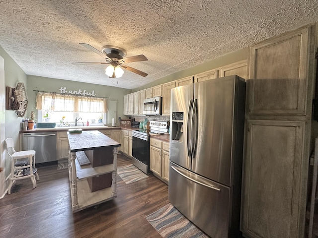 kitchen with a ceiling fan, a textured ceiling, appliances with stainless steel finishes, a sink, and dark wood-type flooring