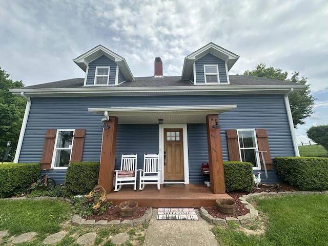 view of front facade featuring a shingled roof, covered porch, and a chimney