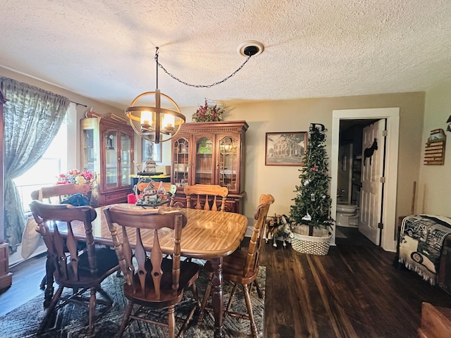 dining room with an inviting chandelier, a textured ceiling, and dark wood finished floors
