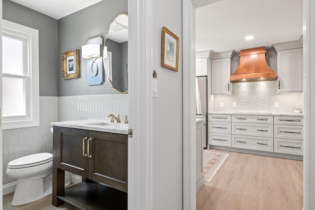 bathroom with tasteful backsplash, wood finished floors, vanity, a wainscoted wall, and toilet