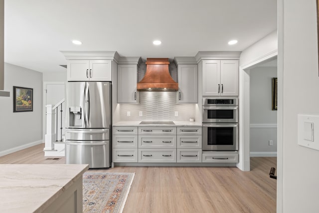 kitchen featuring backsplash, appliances with stainless steel finishes, light wood finished floors, and custom range hood