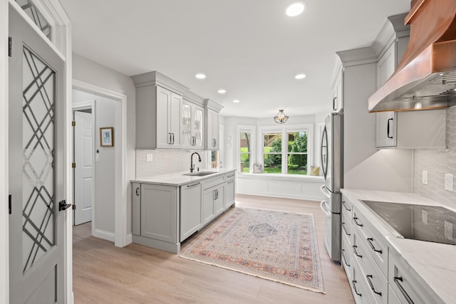 kitchen featuring freestanding refrigerator, black electric stovetop, wall chimney exhaust hood, a sink, and light wood-style flooring