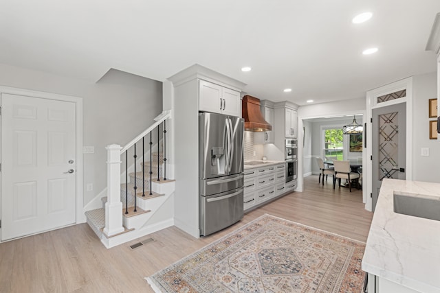 kitchen featuring visible vents, custom exhaust hood, light wood-style floors, light stone counters, and stainless steel appliances