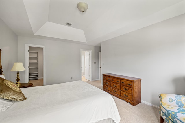 bedroom featuring baseboards, a raised ceiling, a spacious closet, and light carpet
