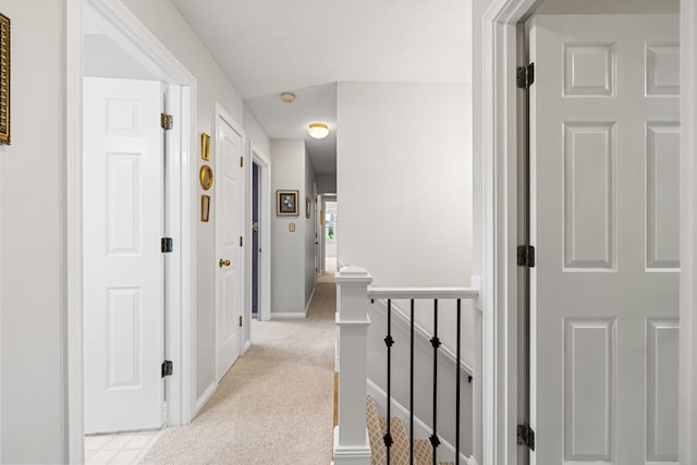 hallway with baseboards, light carpet, and an upstairs landing