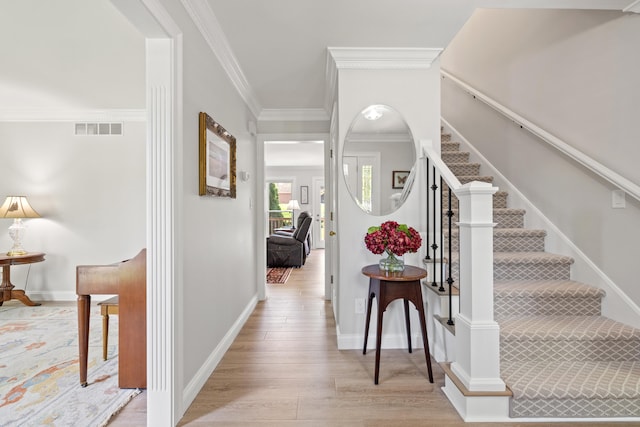foyer with visible vents, crown molding, wood finished floors, baseboards, and stairway