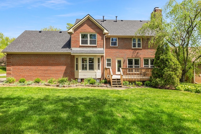 back of property featuring a wooden deck, a chimney, brick siding, a shingled roof, and a yard