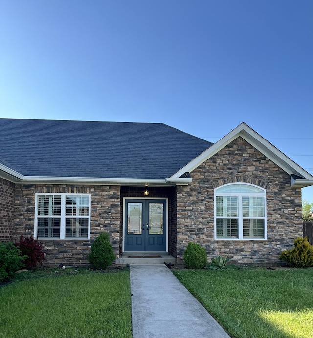 doorway to property featuring roof with shingles, a yard, french doors, and stone siding