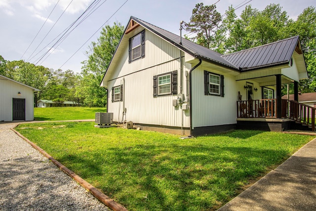 view of side of home featuring central AC unit, covered porch, a yard, and metal roof
