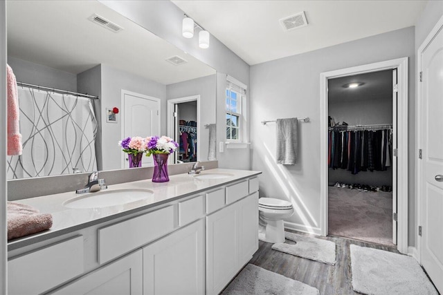 full bathroom with a sink, double vanity, toilet, wood finished floors, and visible vents