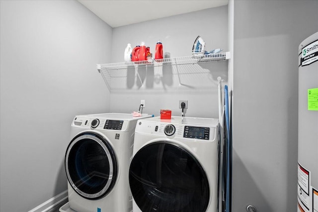 washroom featuring water heater, baseboards, laundry area, and washer and clothes dryer