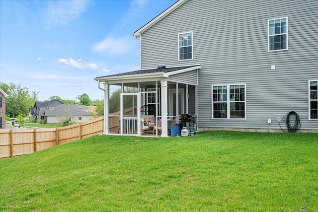 back of property featuring fence, a lawn, and a sunroom