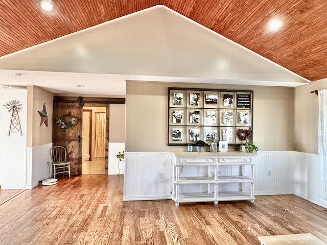 interior space featuring a barn door, a wainscoted wall, wooden ceiling, wood finished floors, and vaulted ceiling