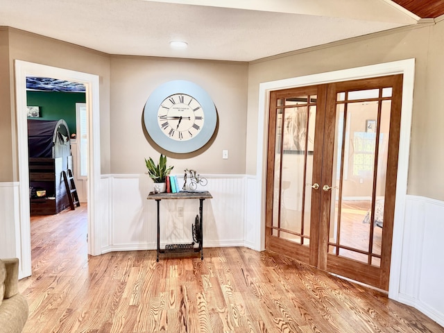 foyer with french doors, ornamental molding, wainscoting, and wood finished floors